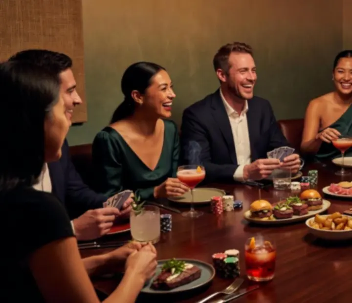 Group gathered around a poker table with shared plates and drinks in a dark restaurant